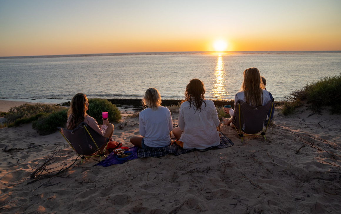 Group of friends sitting and eating on a Ningaloo beach at sunset